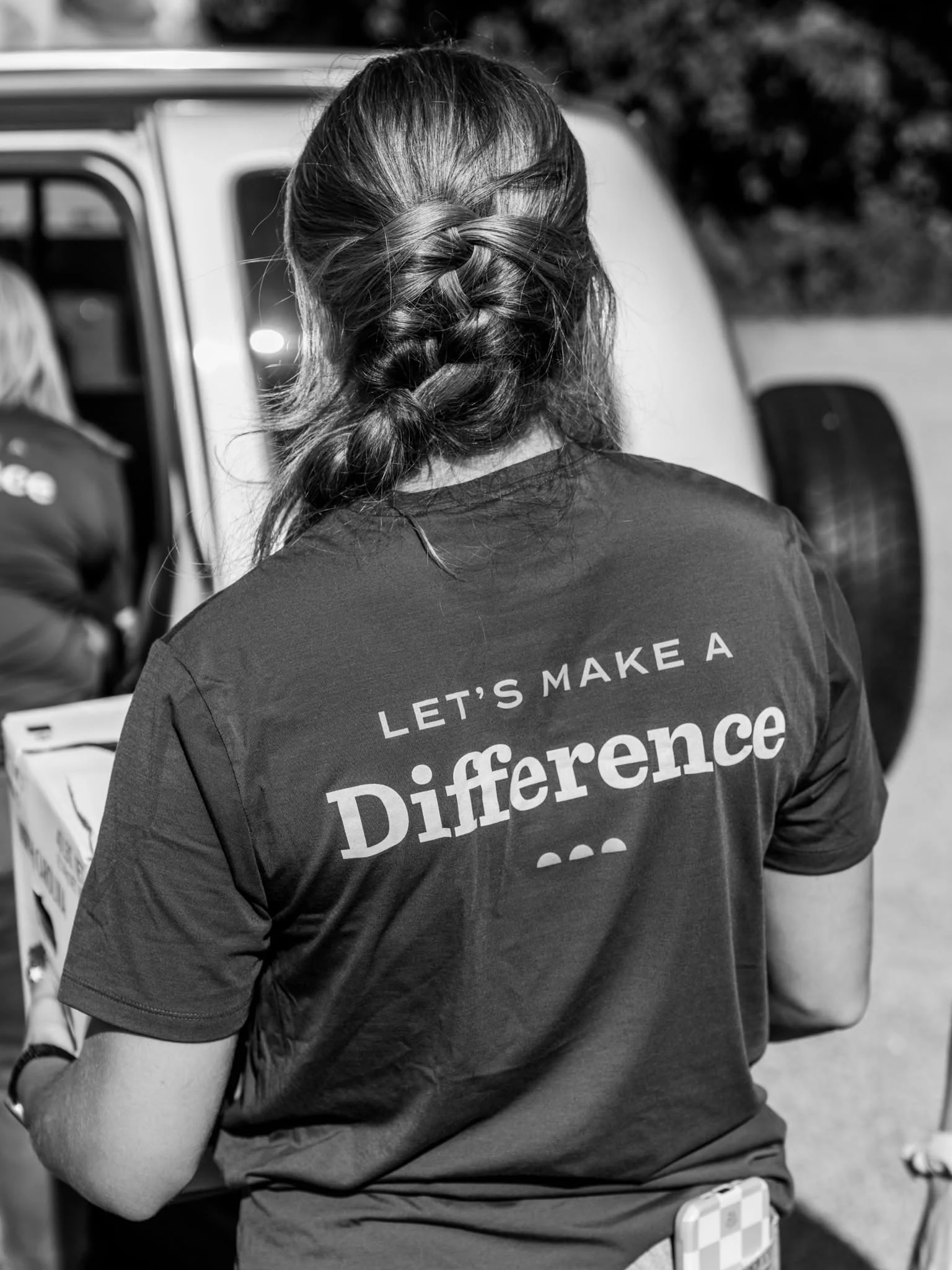 A braided volunteer wears a shirt reading ‘Let’s Make a Difference’ at a food distribution.