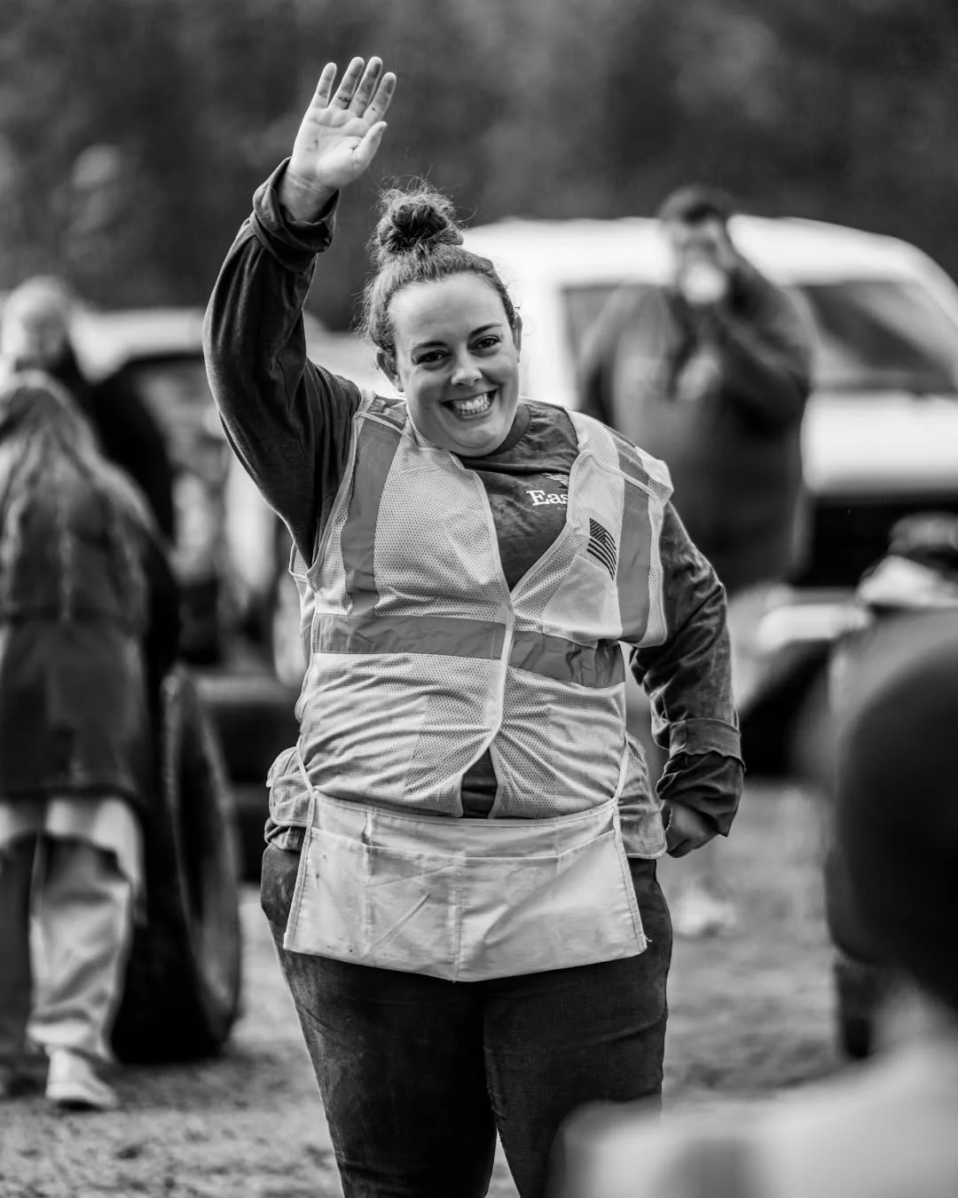 A volunteer in a safety vest waves in a parking lot.