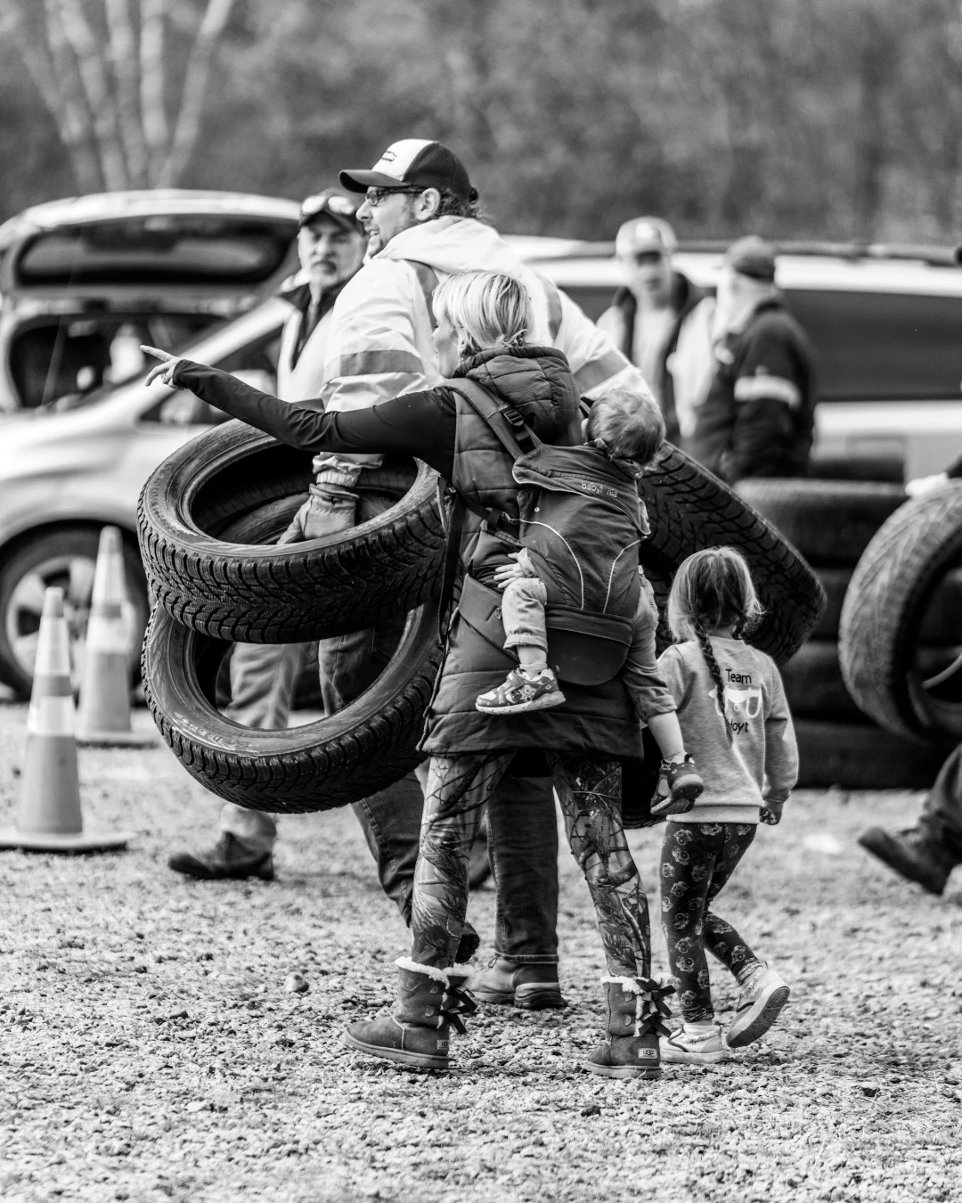 A volunteer carries a stack of tires while another works nearby.
