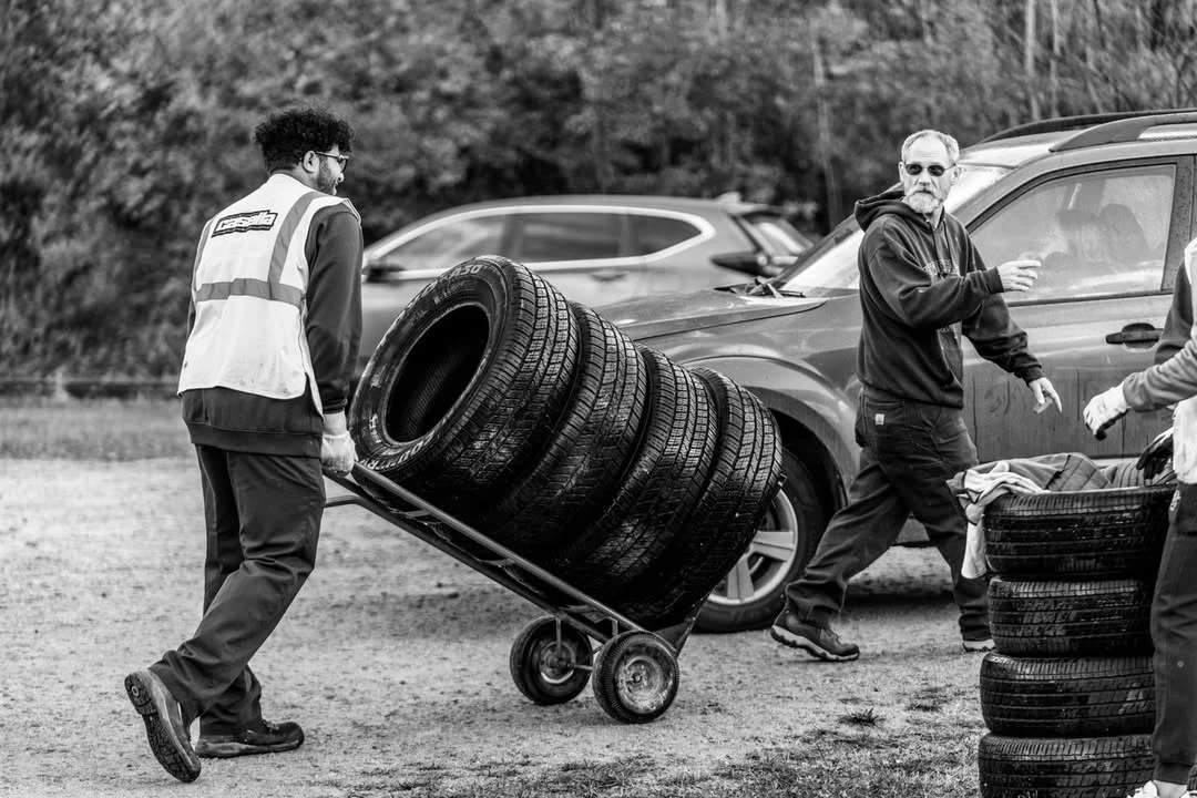 Two volunteers move a stack of tires on a hand truck.