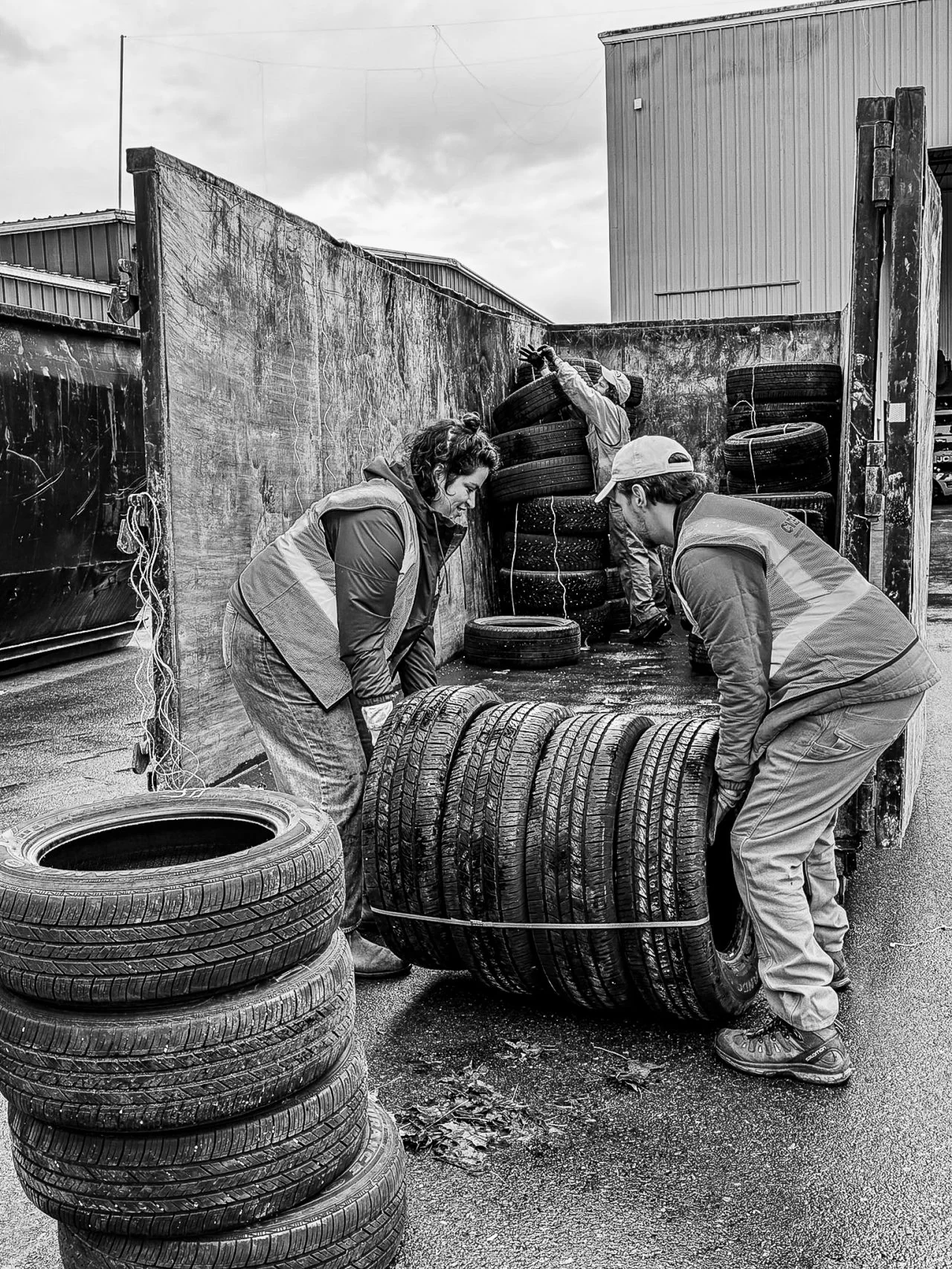 Two volunteers handle tires beside an open trailer in the rain.