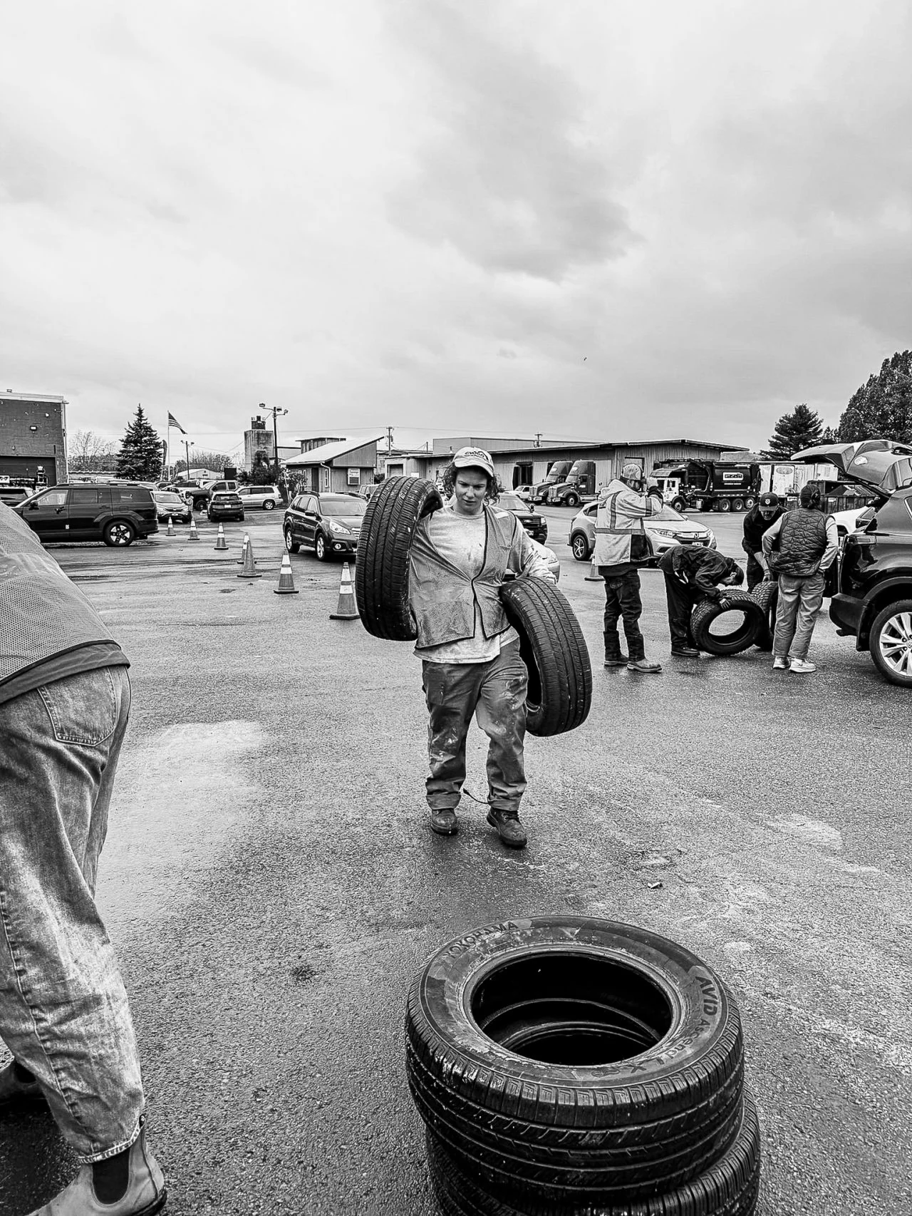 A volunteer walks toward a donated tire in a wet parking lot.