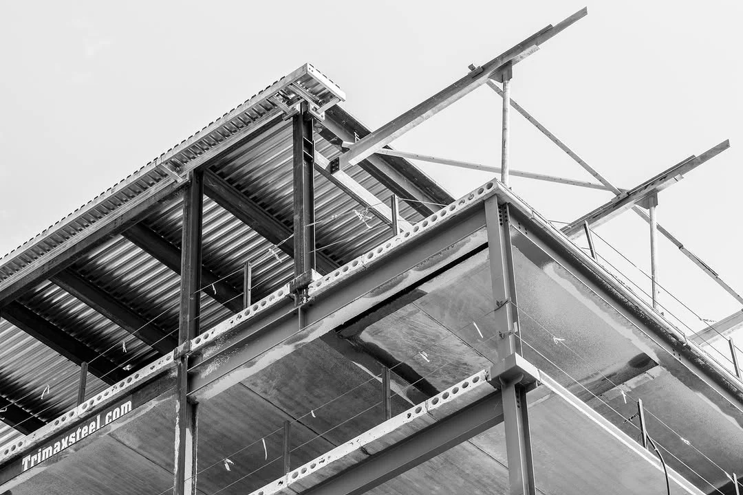 An unfinished steel building frame rises above a construction fence.