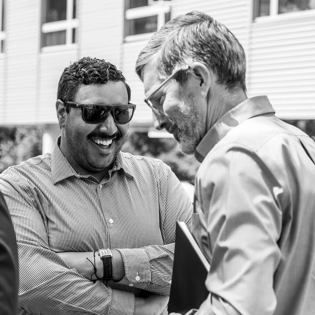 Two men smile while talking at the outdoor groundbreaking.