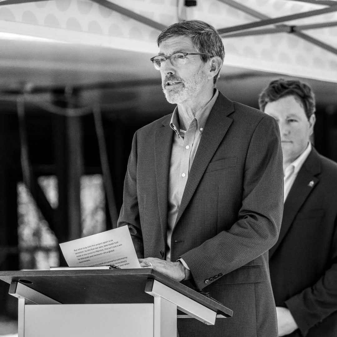 A man reads from notes while speaking at an outdoor lectern.