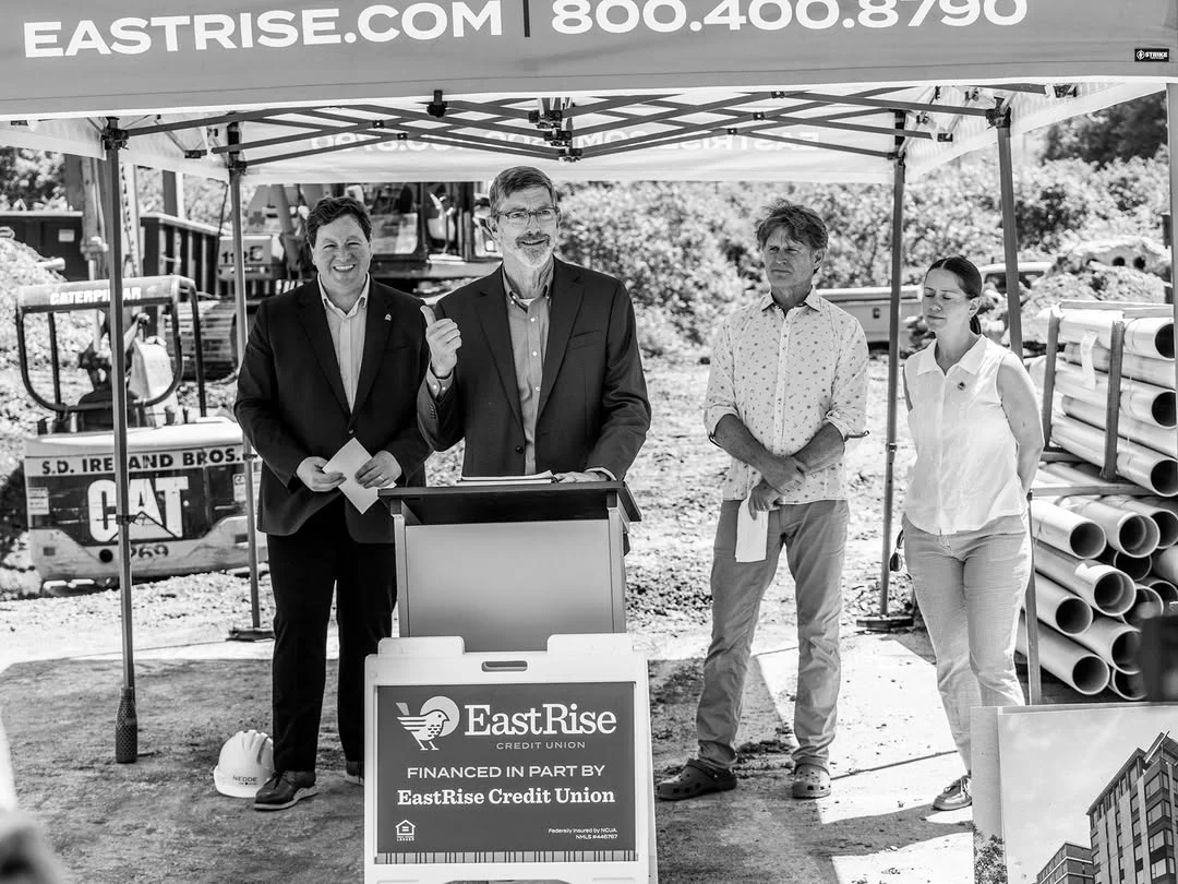 Three people pose beside an EastRise lectern at the construction site.