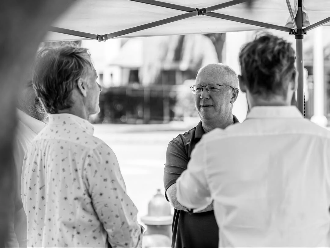 A man wearing glasses speaks with two attendees under the event tent.