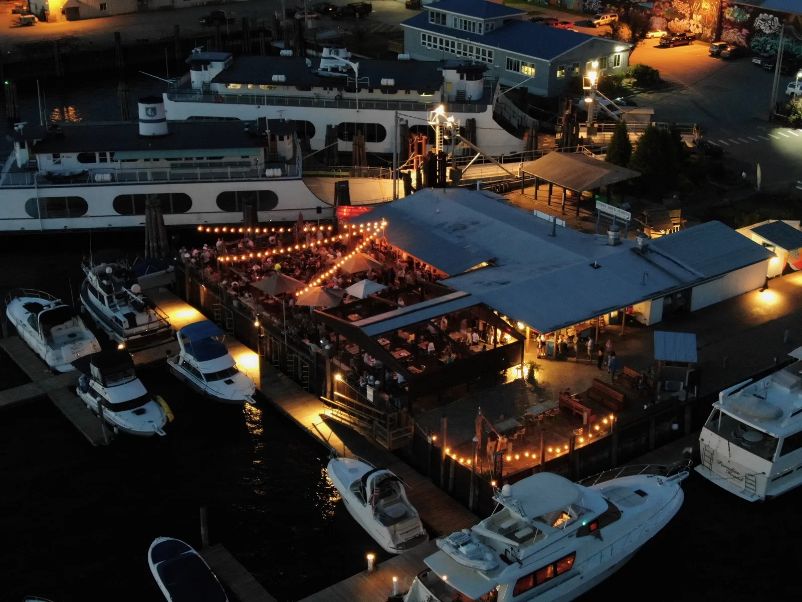 Waterfront restaurant and marina glowing at dusk with boats moored around the docks