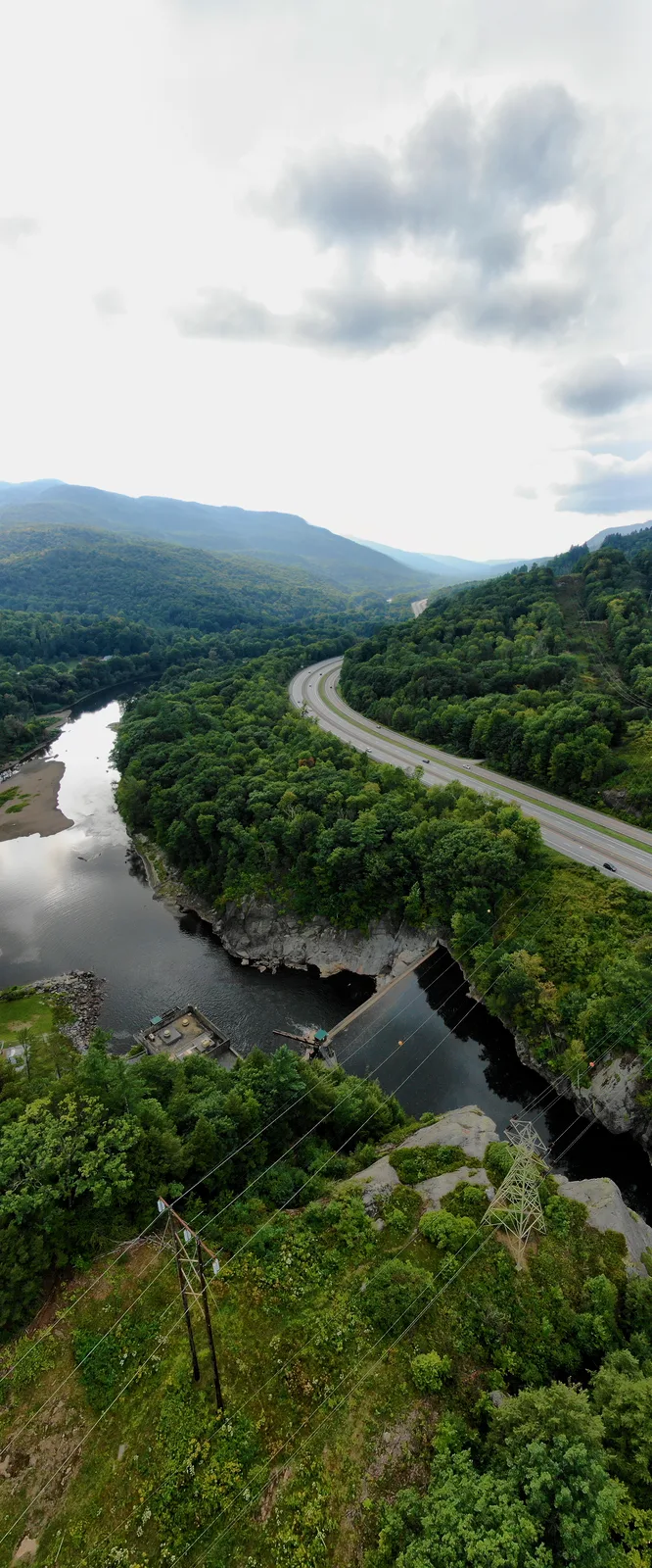 Vertical aerial panorama of a river winding between forested hills and a parallel road