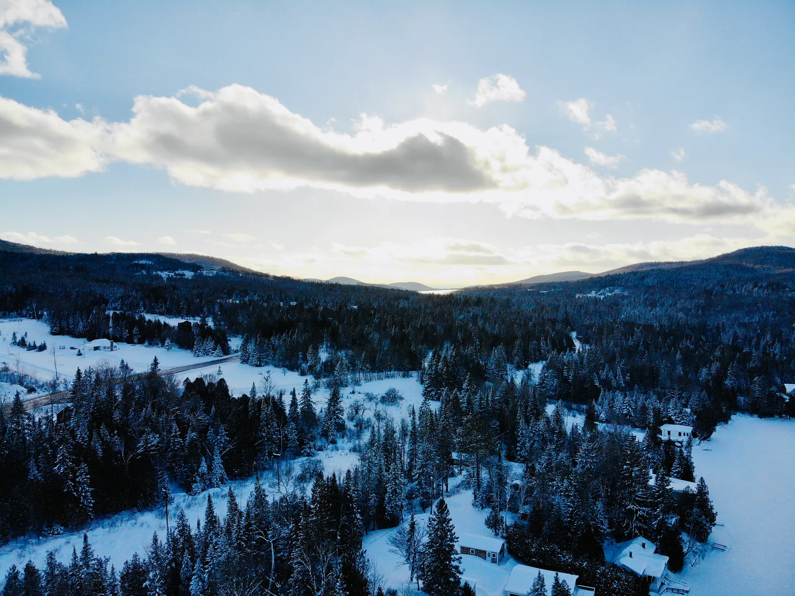 Snow-covered valley, wooded hills, and scattered homes under low winter sunlight