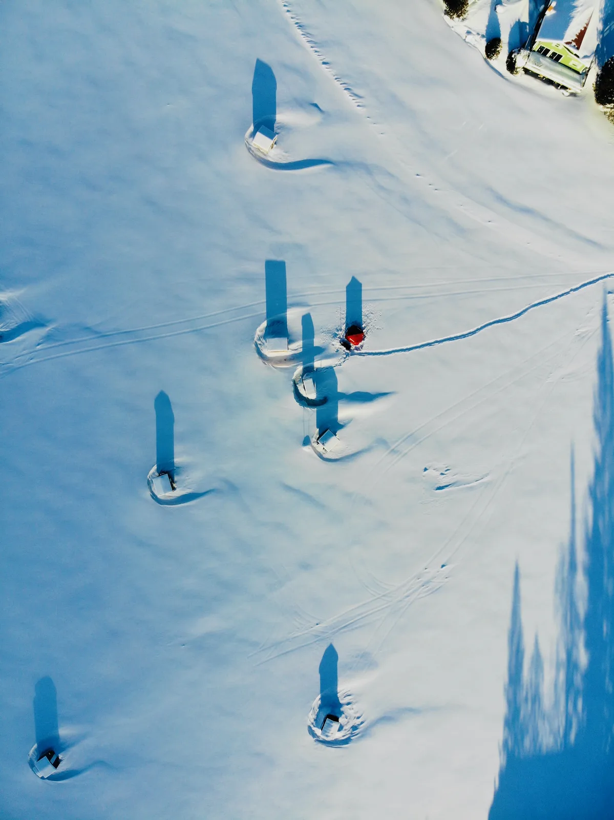 Top-down view of small shelters casting long shadows across a snow-covered frozen lake