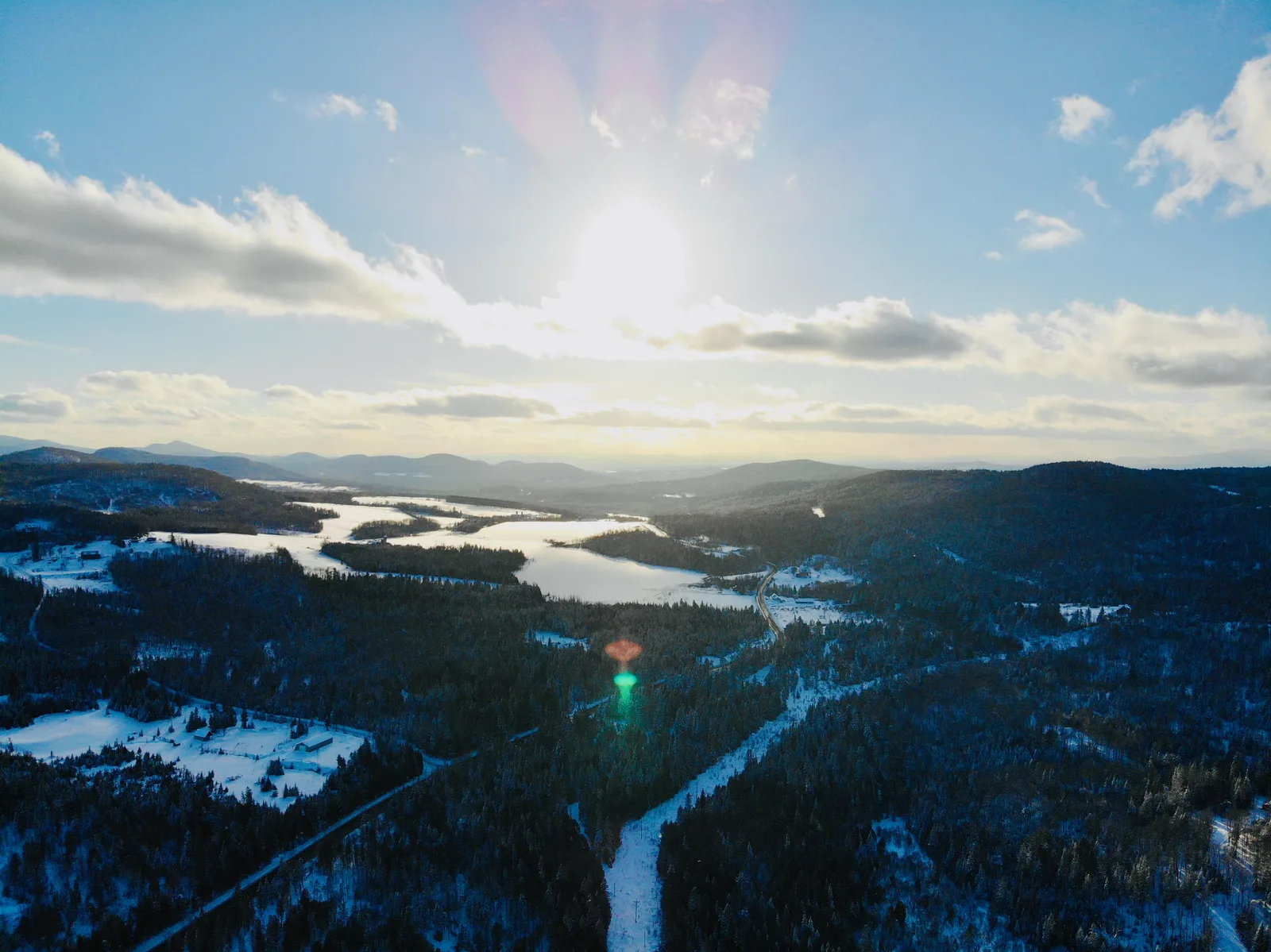 Low winter sun above snow-covered valleys, wooded ridges, and distant lakes