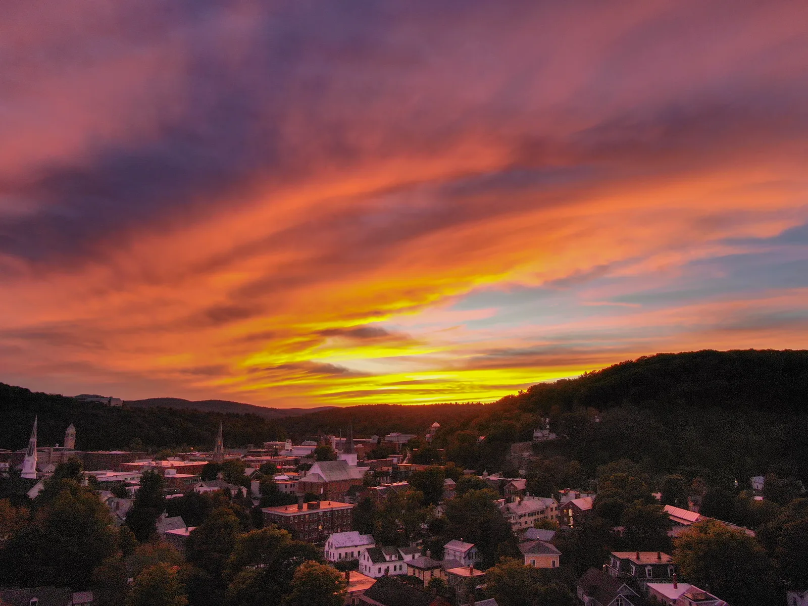 Red and orange sunset spreading above a small town and dark wooded hills