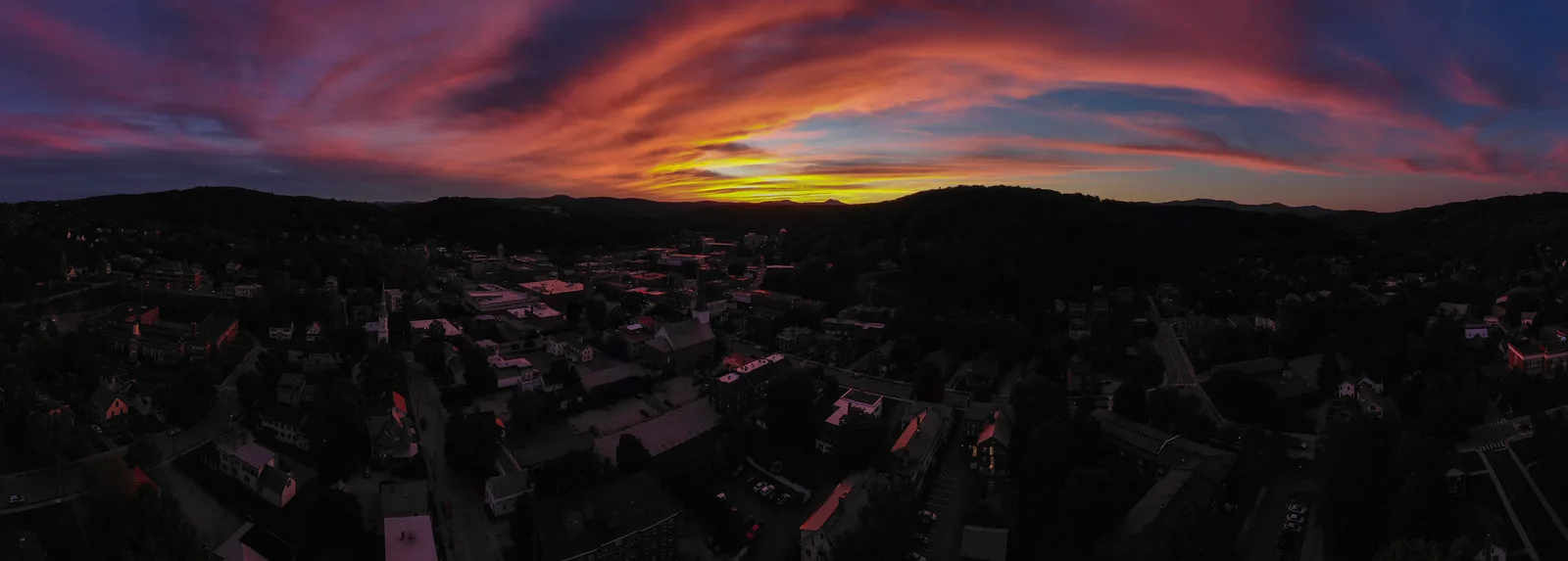 Dark aerial panorama of a town silhouetted beneath a vivid red sunset