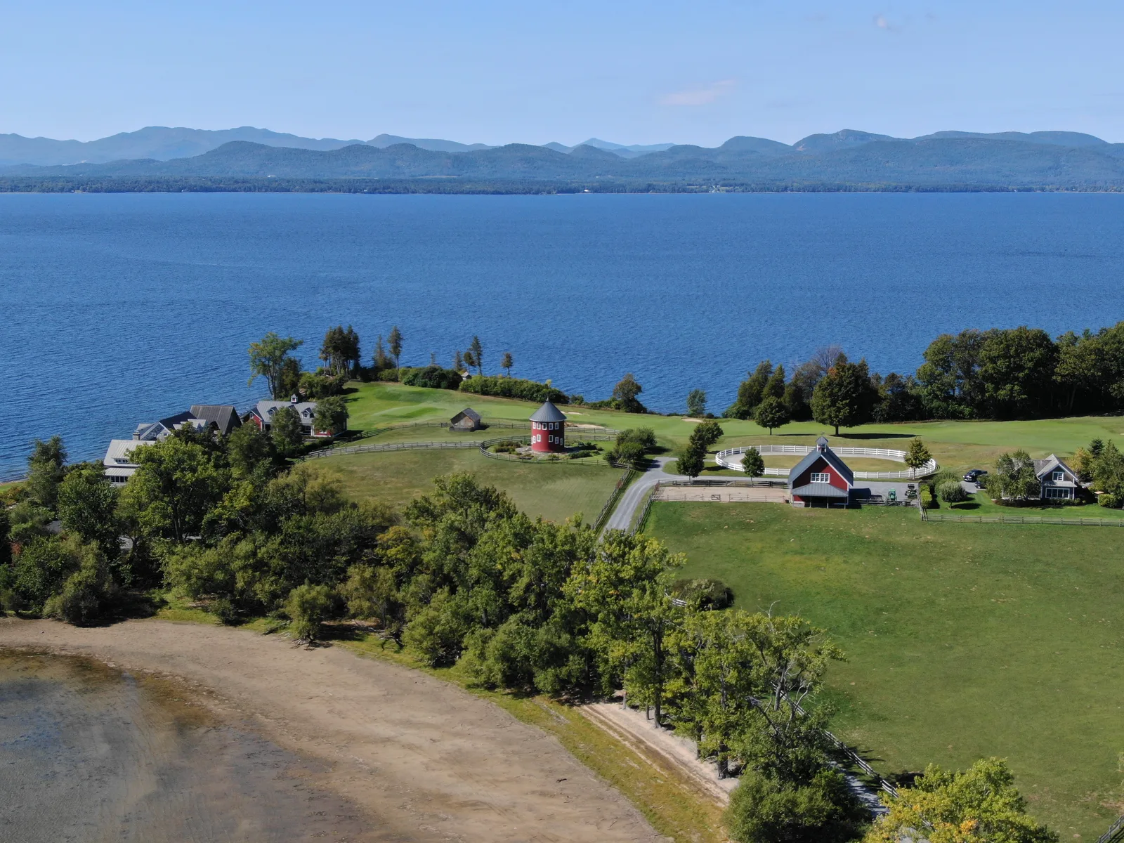 Lakeside property, green fields, and blue water with mountain ridges on the horizon