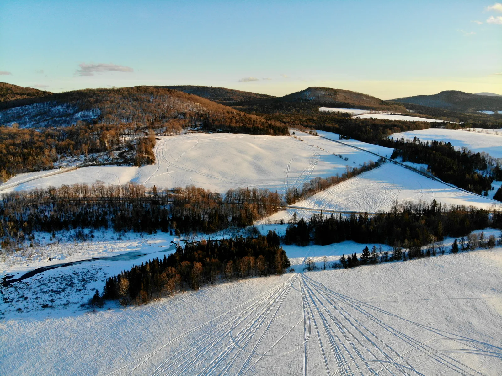 Snow-covered fields divided by hedgerows and forested ridges in late afternoon light