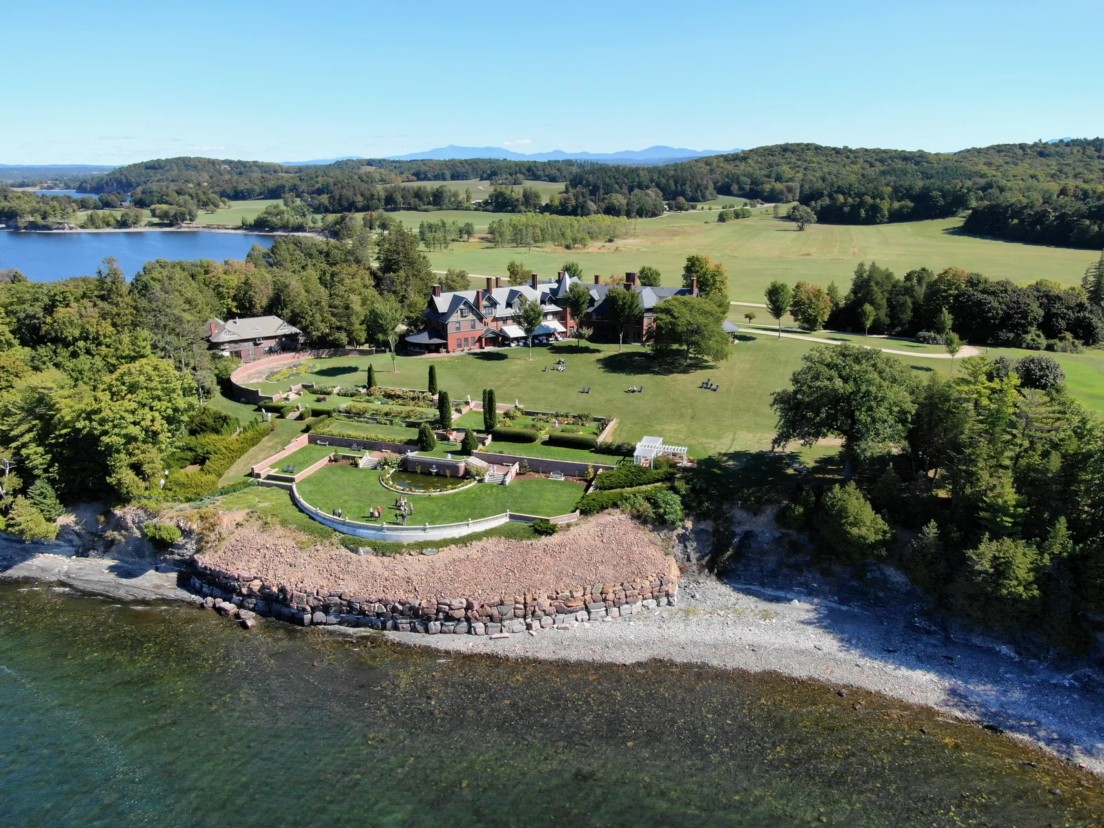 Formal gardens and historic buildings on a green lakeshore viewed from above