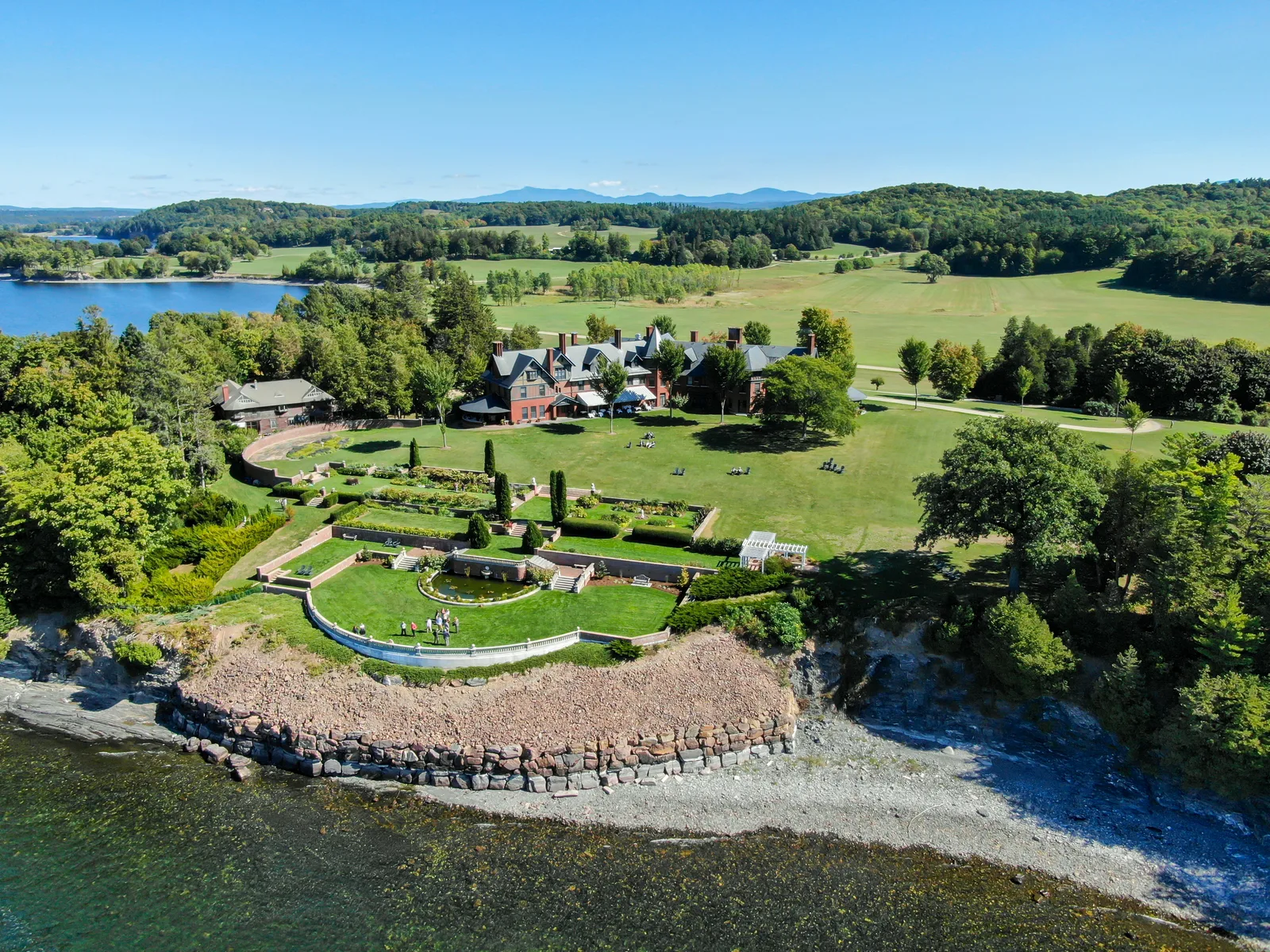 Wide aerial view of formal gardens, fields, and buildings along a rocky lakeshore