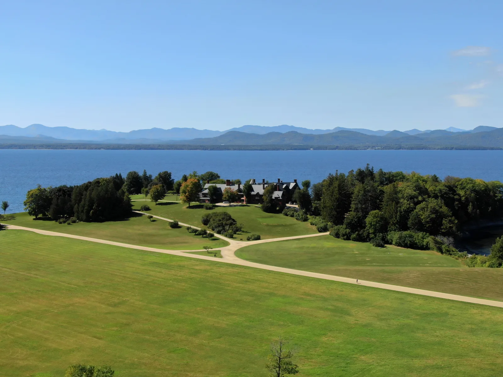 Broad green lawn descending toward a blue lake with mountains beyond