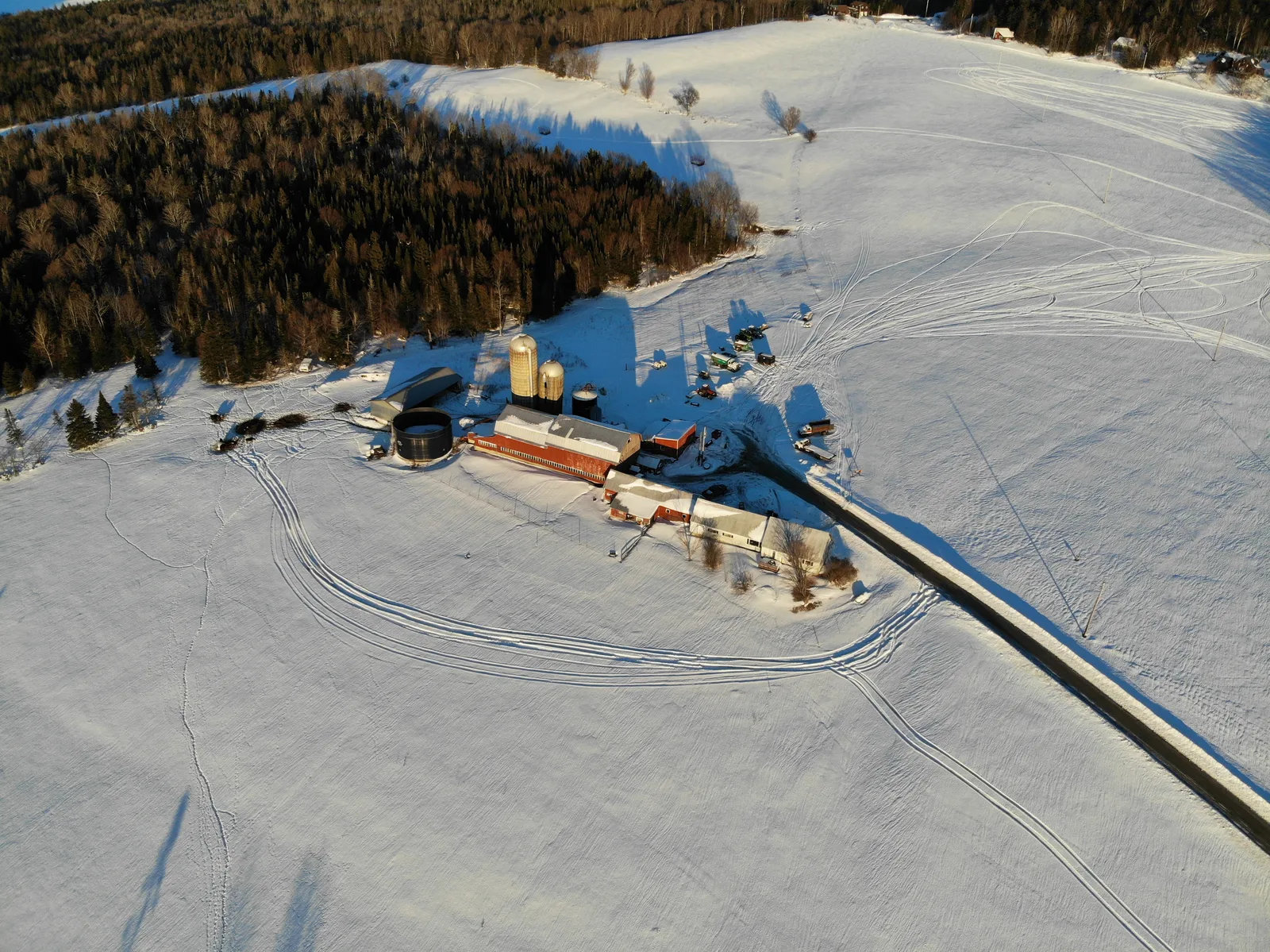 Isolated buildings and a plowed road surrounded by expansive snow-covered fields