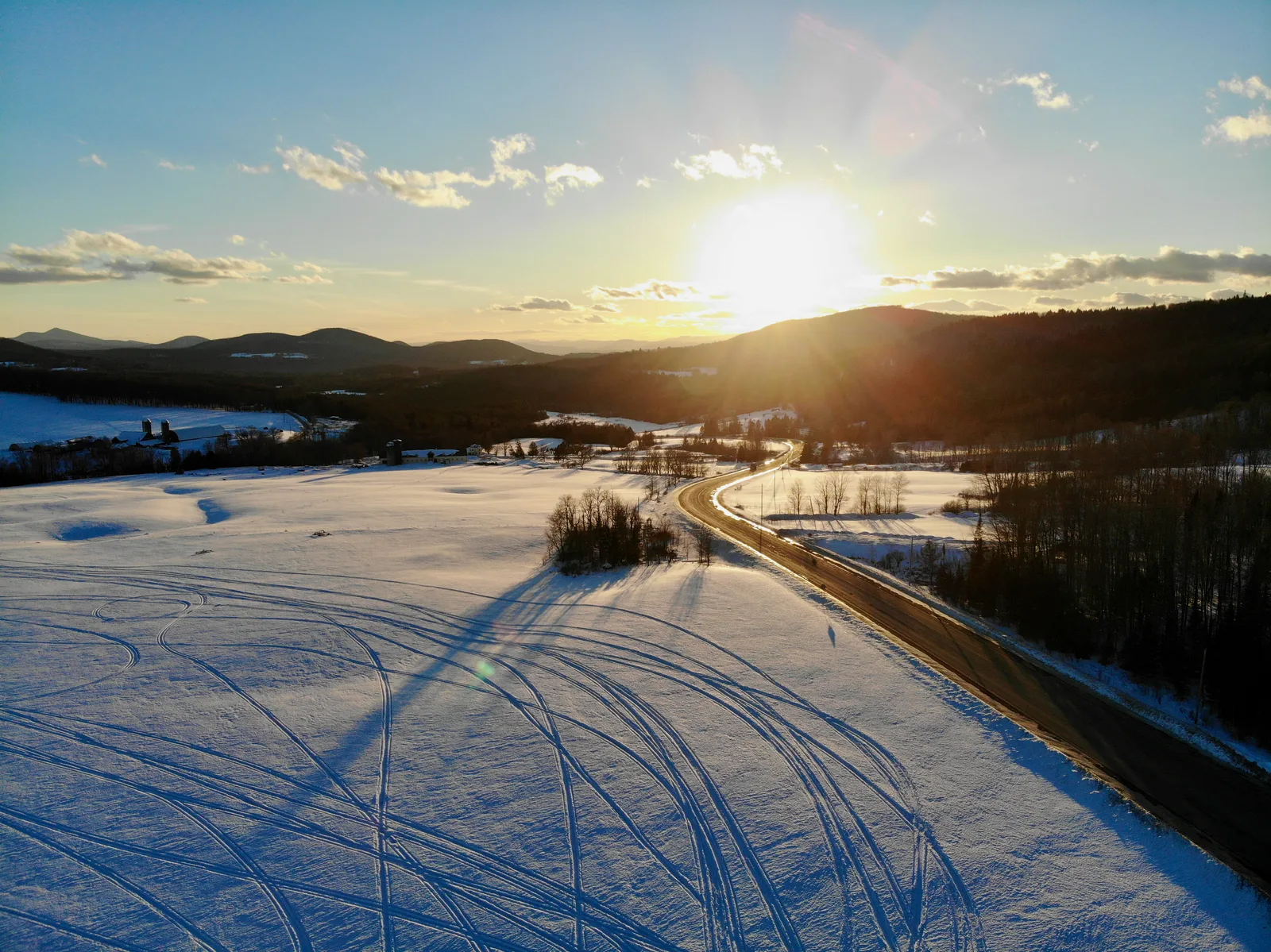 Low sun casting long shadows across a snow-covered field marked by vehicle tracks