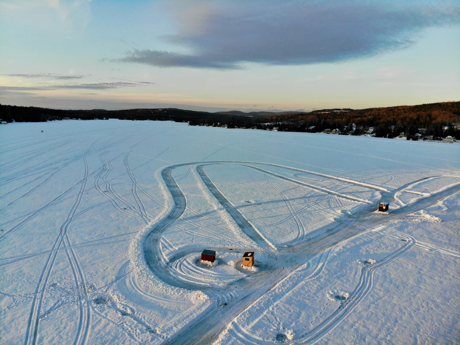 Curving cleared tracks and small shelters on a frozen lake at dusk