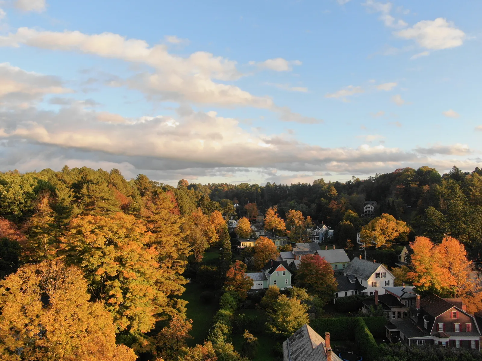 Homes surrounded by dense orange and gold foliage beneath a partly cloudy sky