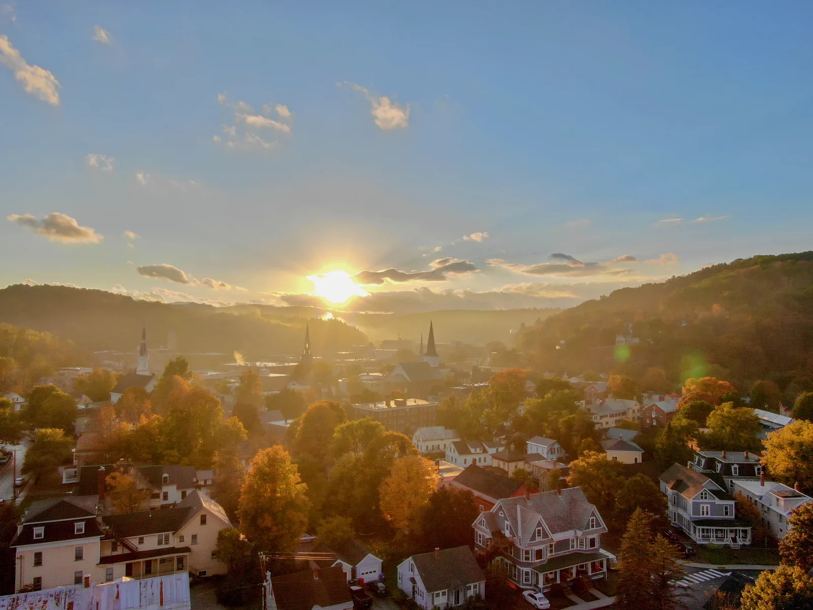 Low sun shining over an autumn town with church steeples and wooded hills