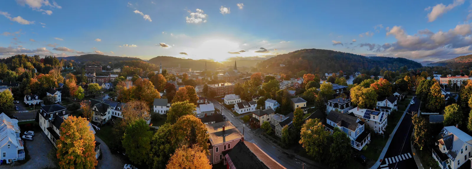 Panoramic aerial view of a small town surrounded by autumn foliage and rolling hills