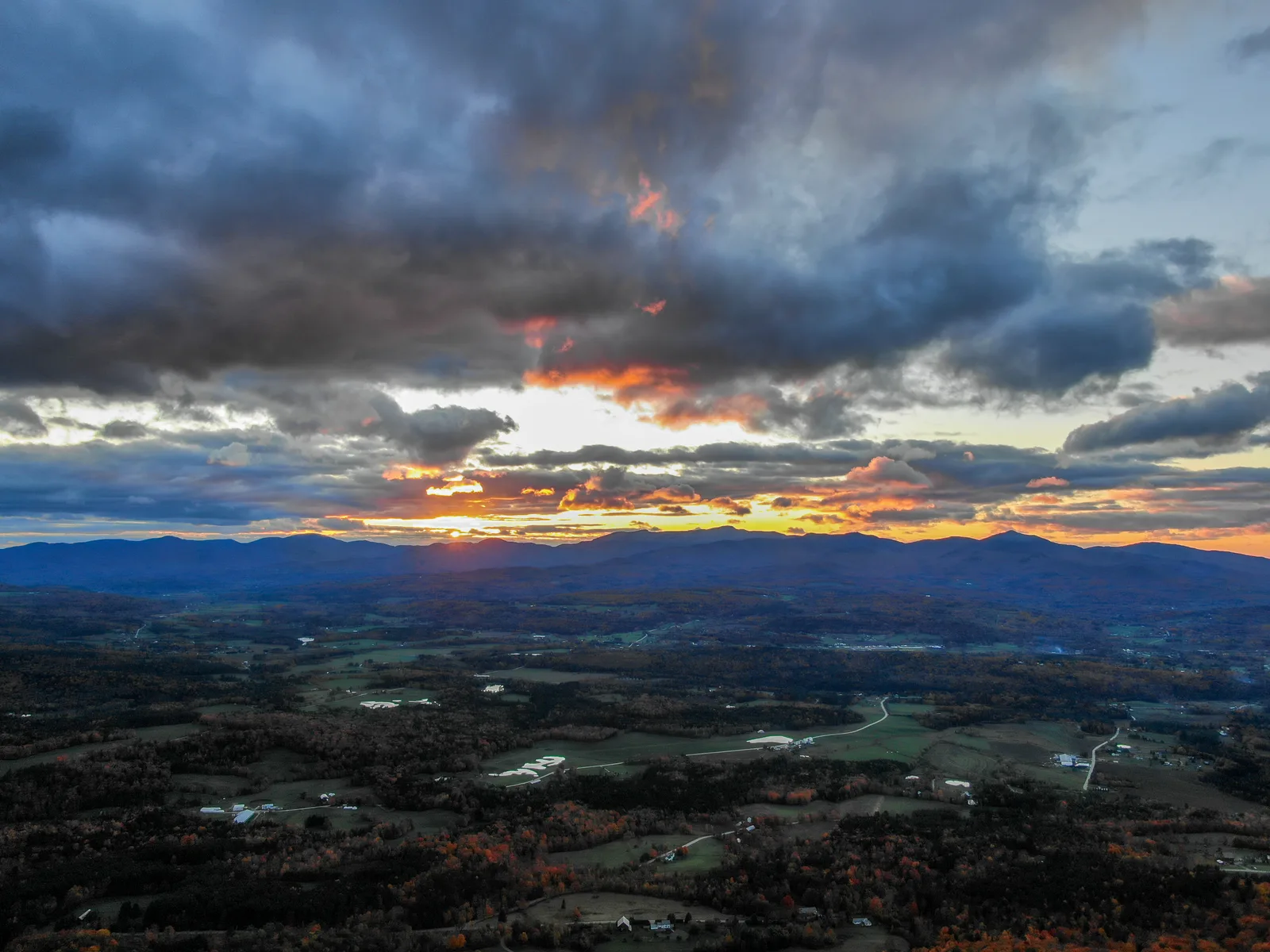 Orange sunset breaking beneath dark clouds over a wide mountain valley