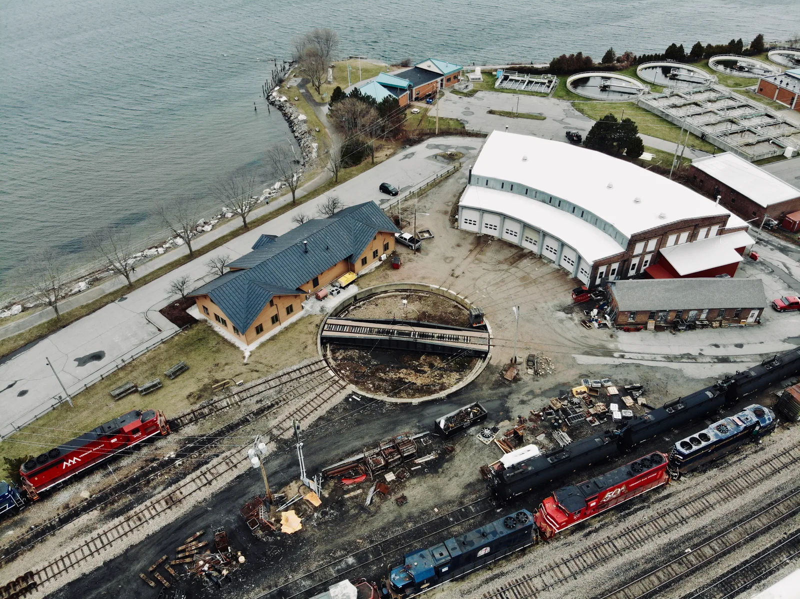 Waterfront rail yard with a roundhouse, maintenance buildings, and parked trains