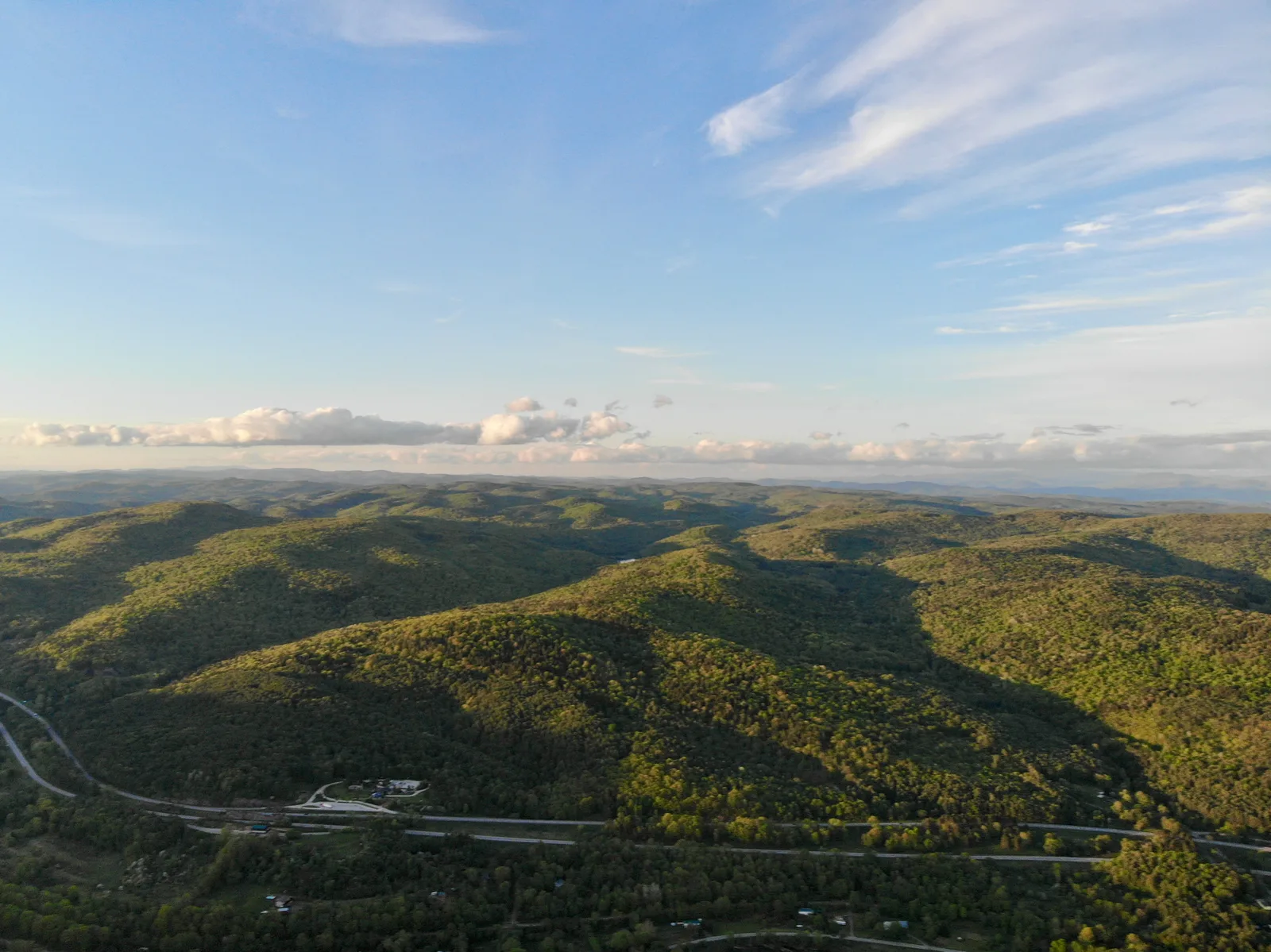 Green mountain ridges crossed by a highway beneath a bright blue sky