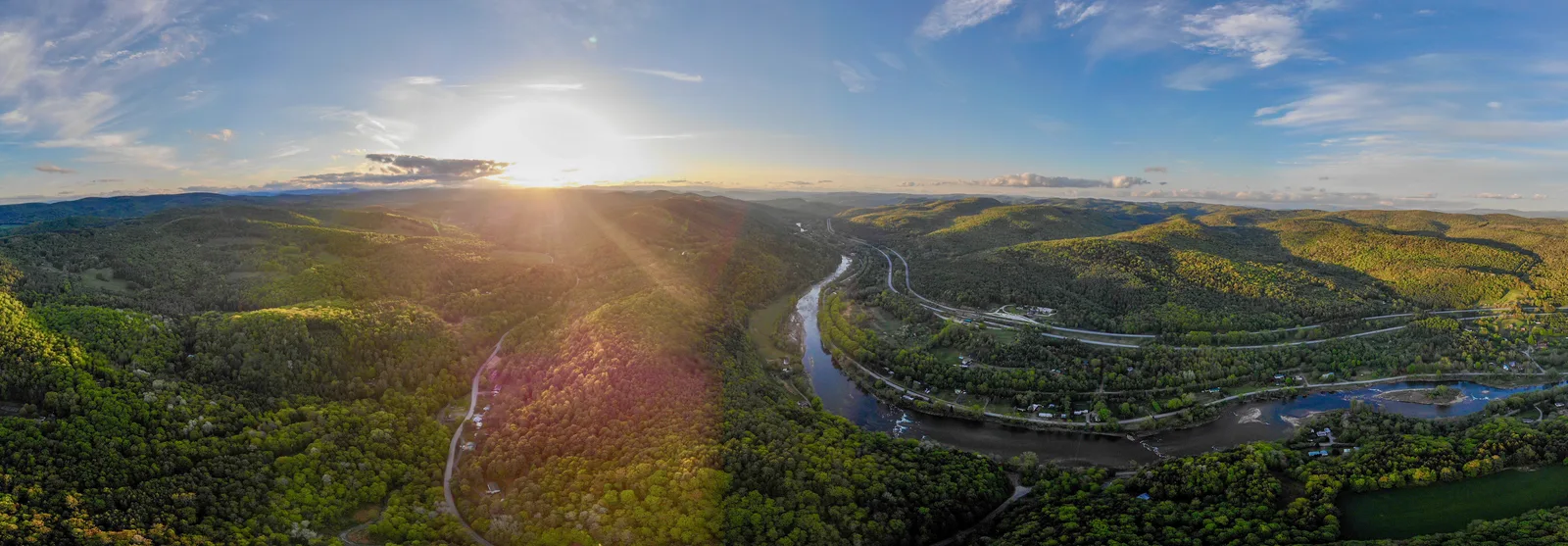 Panoramic aerial view of sunlight over forested mountains and a curving highway