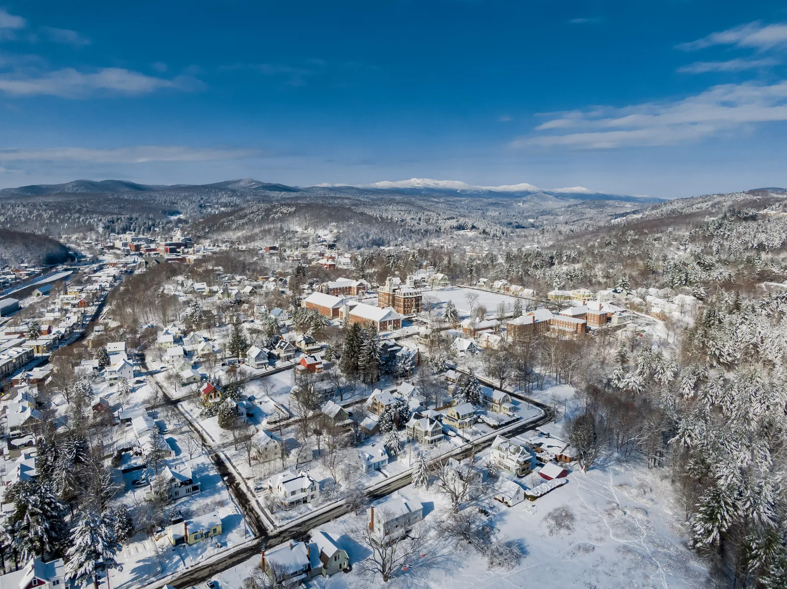 Snow-covered town and surrounding wooded hills beneath a deep blue winter sky