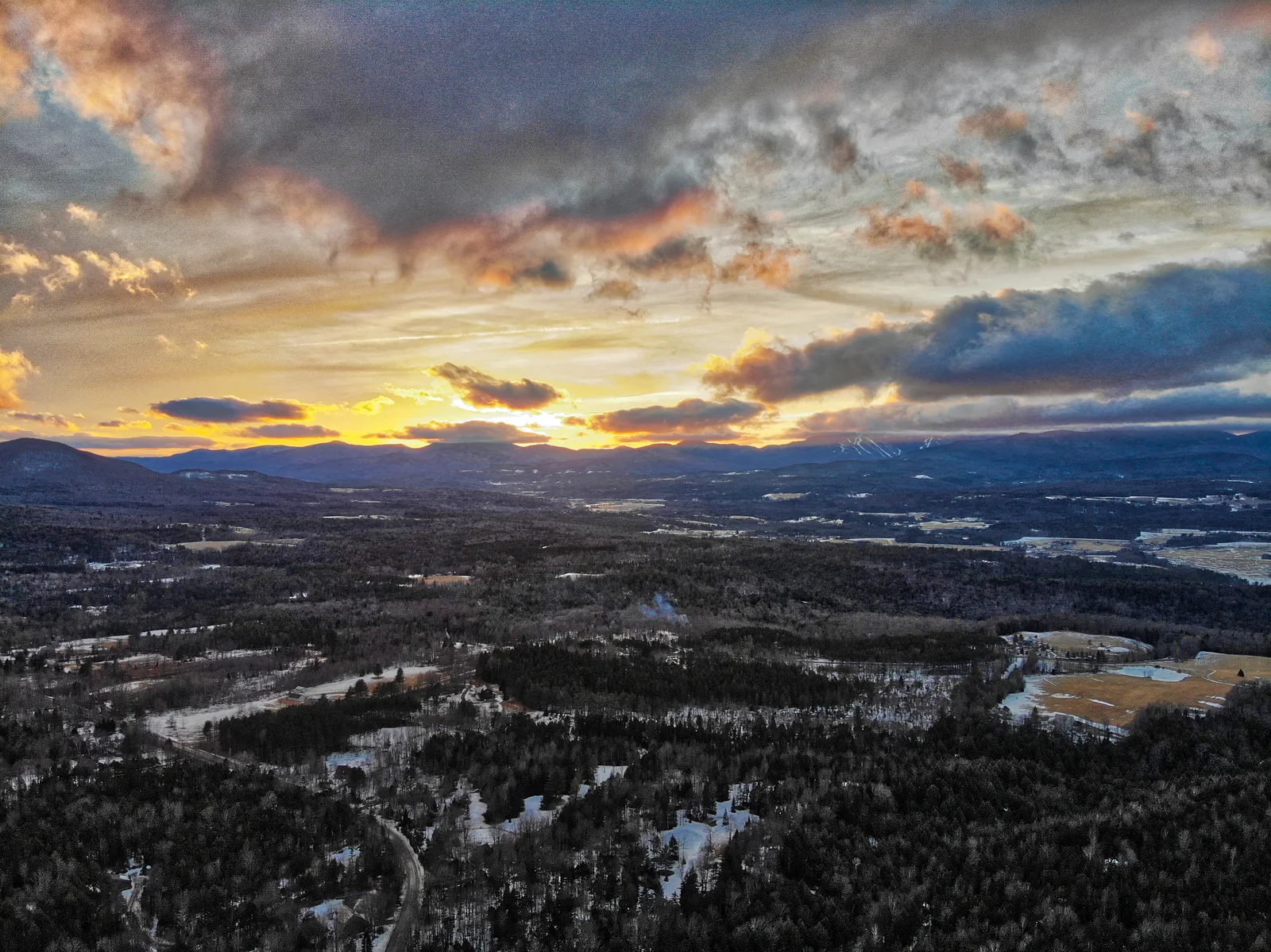 Winter sunset spreading through broken clouds above a snow-covered valley