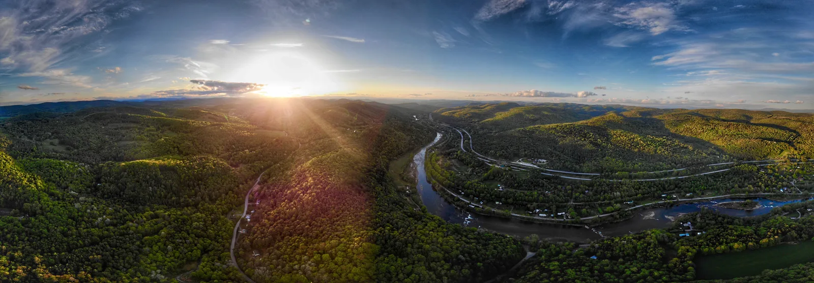 Sunlit panorama of green mountain ridges and a highway curving through the valley