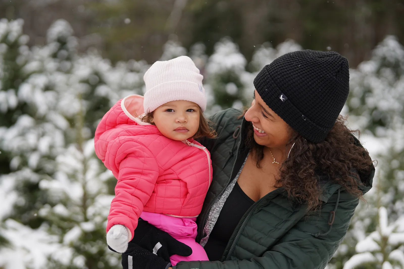 Person in green jacket and black beanie holding child in pink coat and light hat