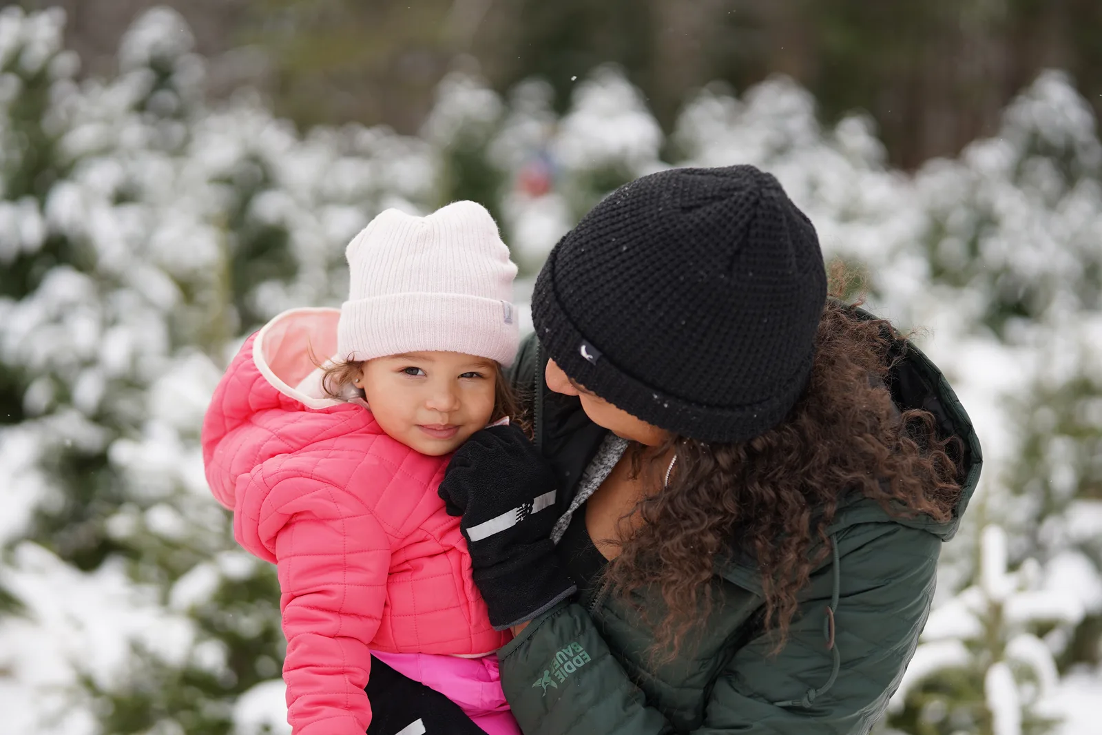 Person in green jacket and black beanie holding child in pink coat and light hat