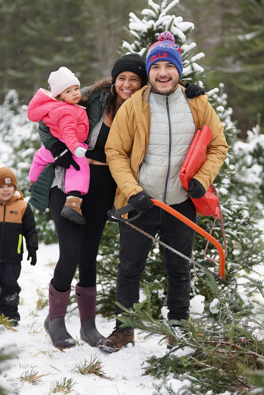 Three adults and a child in pink jacket pose near snow-covered evergreen trees.