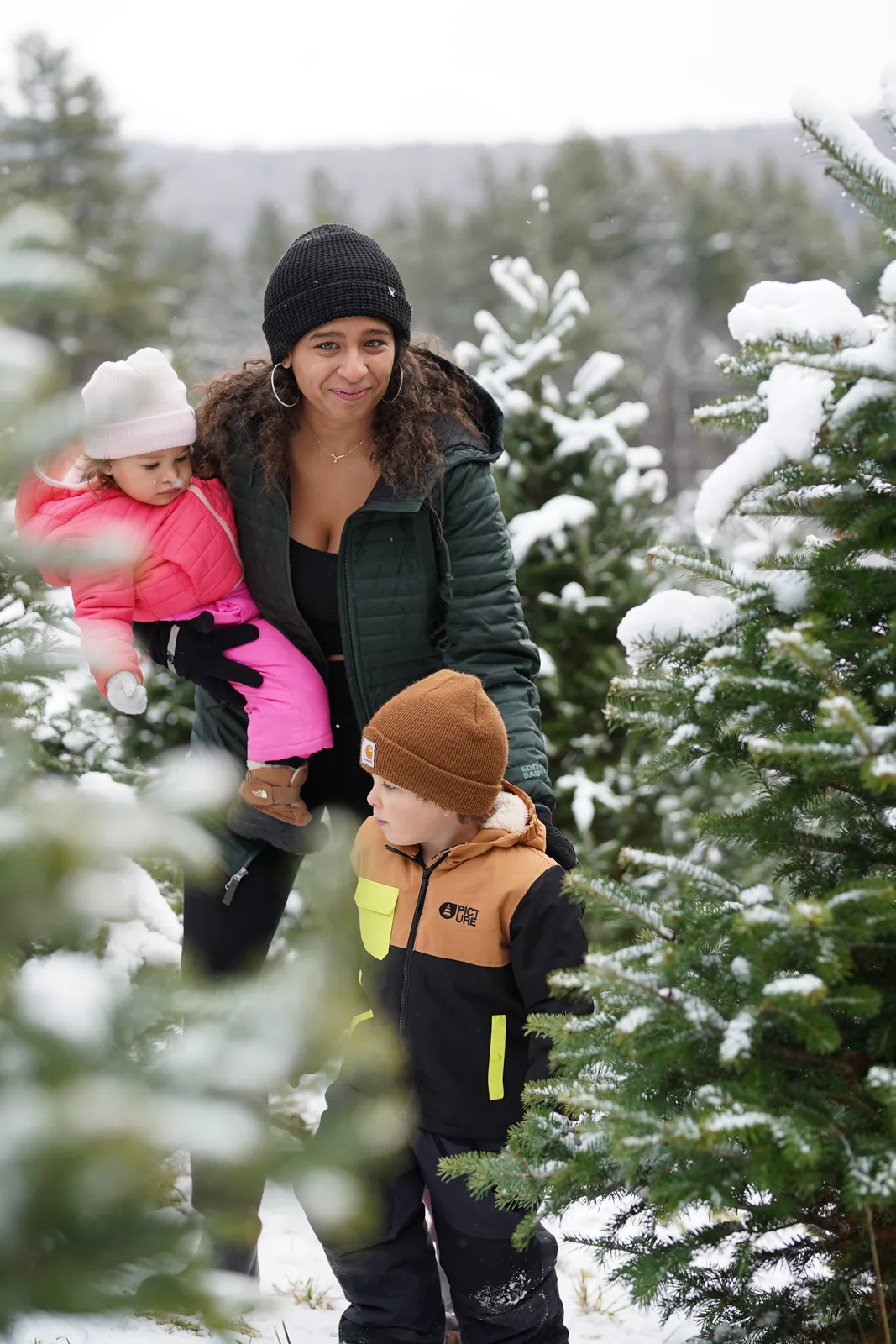 Woman in green jacket holds a child in pink, another child in brown beanie nearby.