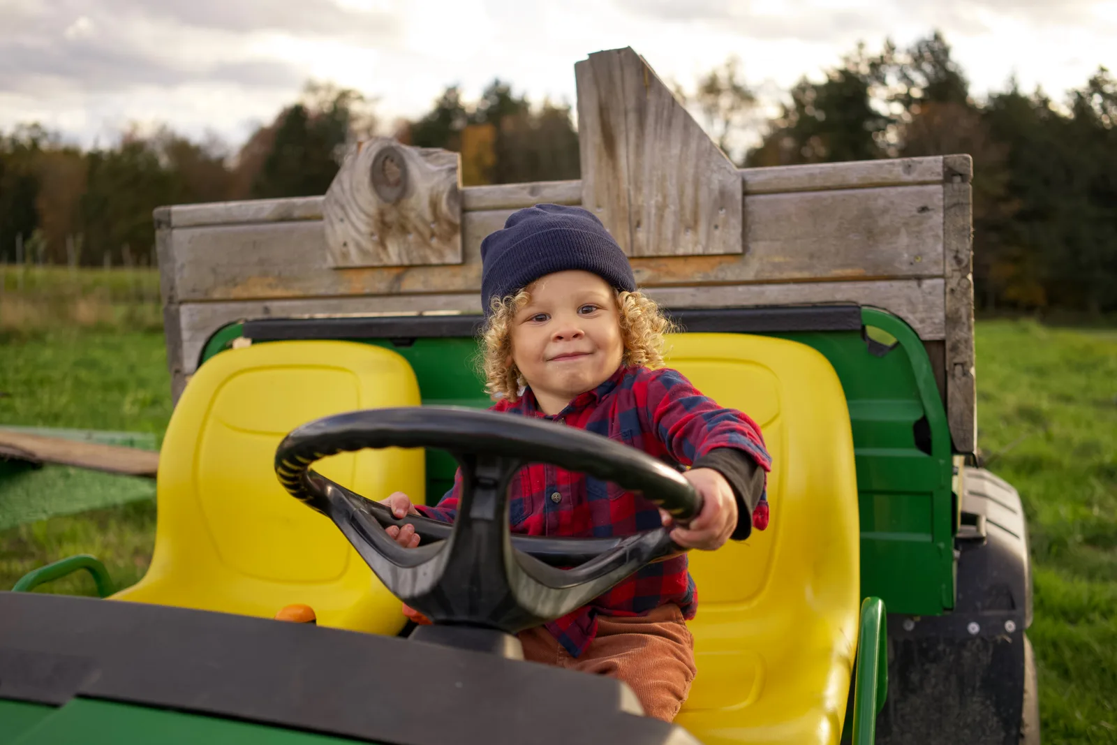 Child in a blue beanie and red plaid shirt holding a tractor steering wheel