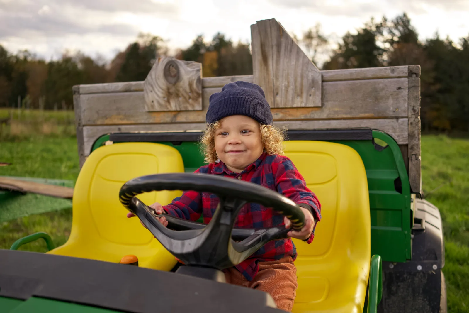 Child in a blue beanie and red plaid shirt sitting on a green tractor