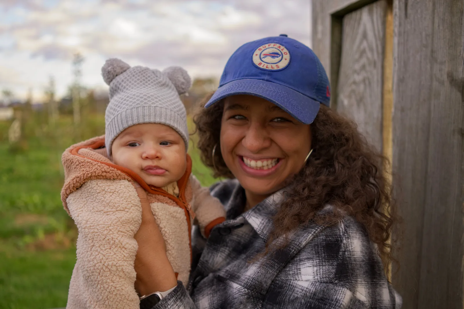 Adult in a blue cap holding a baby in a light gray bear hat and cream jacket