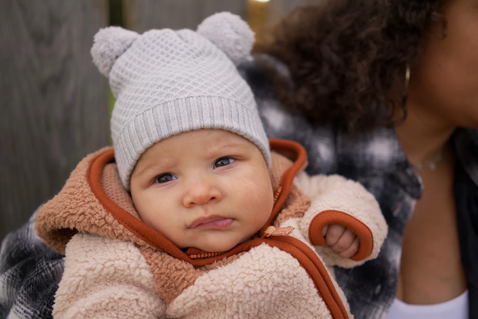 Baby in a light gray knit hat and cream jacket with orange trim held close