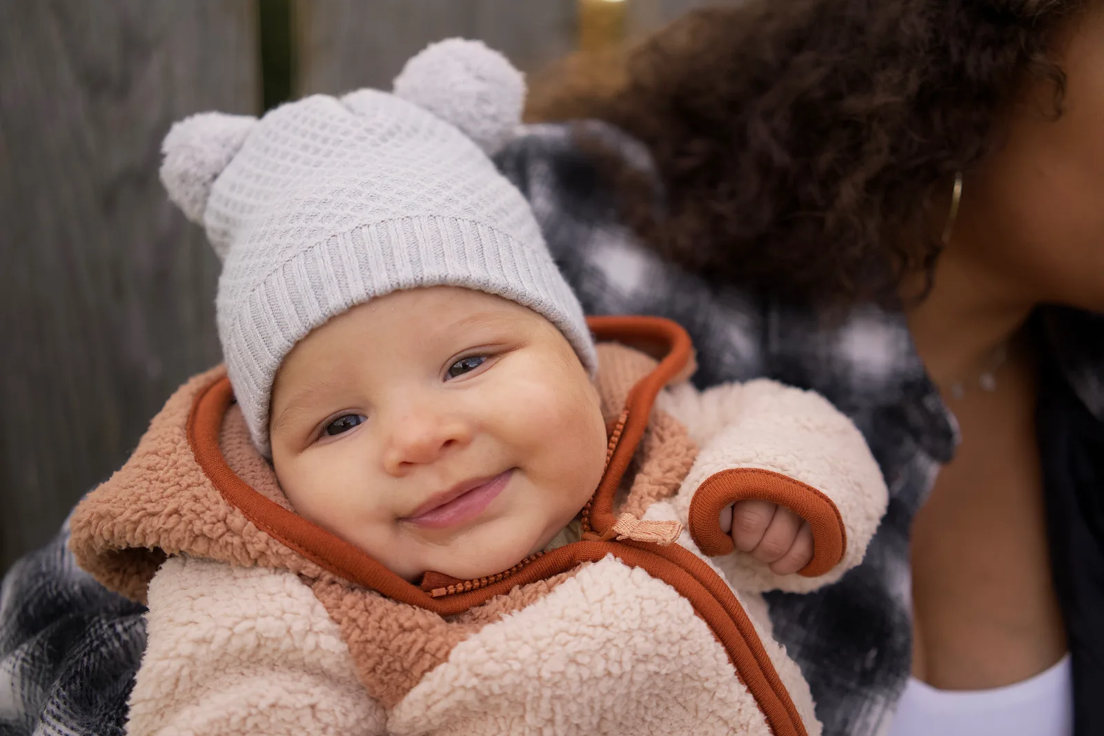 Baby in a light gray knit hat and cream jacket with orange trim smiling