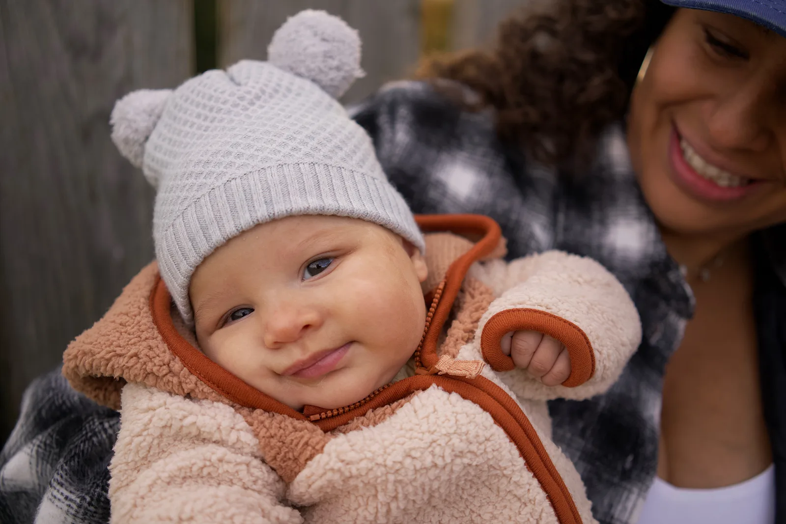 Baby in a light gray knit hat and cream jacket with orange trim looking up