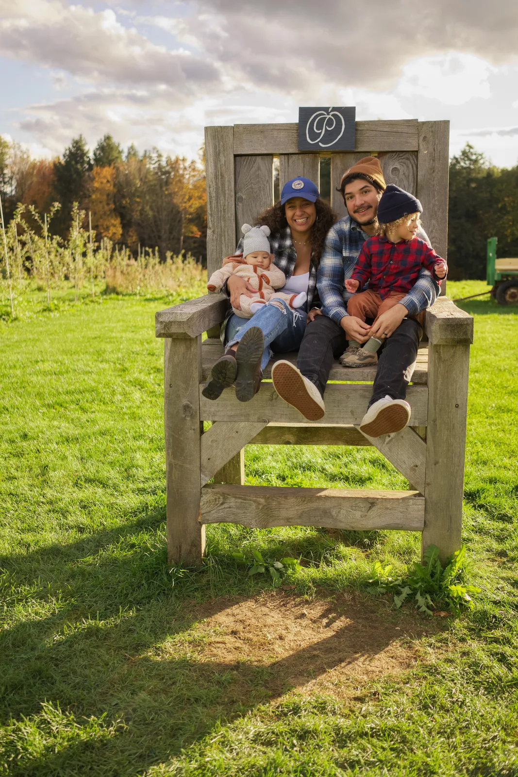 Four people seated on wooden chair with sign above, grassy field and distant trees