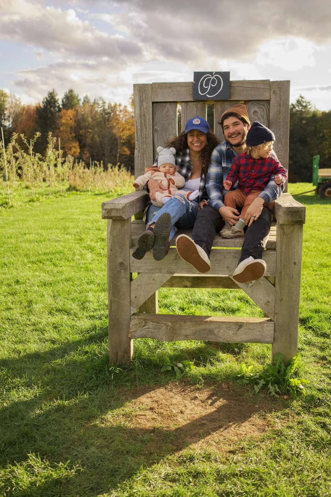 Four people on wooden chair, orchard rows and autumn foliage in background