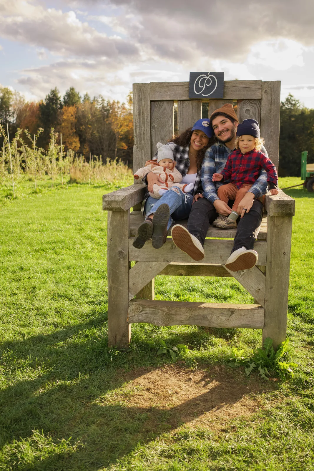 Four people on wooden chair, orchard rows and forested hills in distance