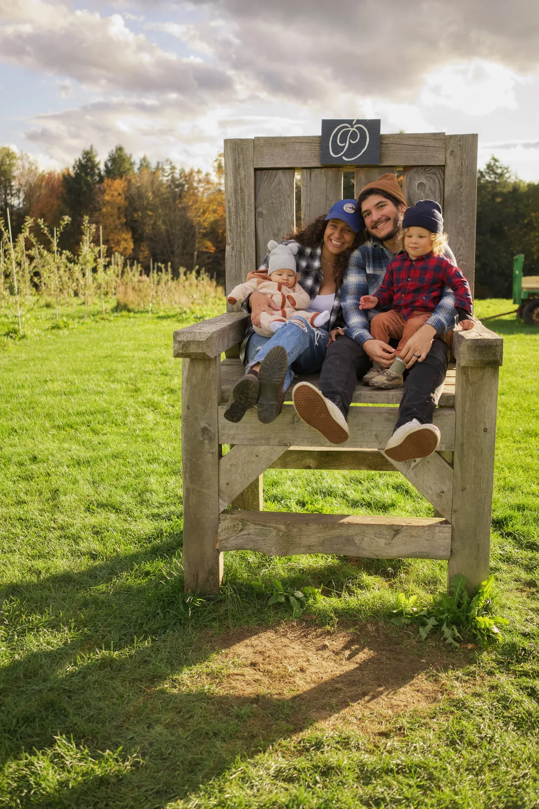 Four people on wooden chair, wide grassy field with scattered clouds